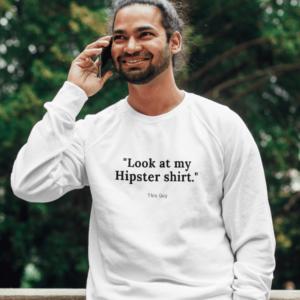 A man with a man bun hairstyle wearing a long sleve shirt that says, '"Look at my Hipster shirt' This Guy"